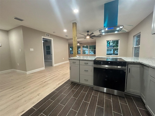 kitchen with light stone counters, visible vents, island range hood, wood finished floors, and range with electric cooktop