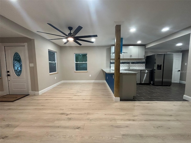 kitchen with stainless steel appliances, a sink, open floor plan, backsplash, and light wood finished floors