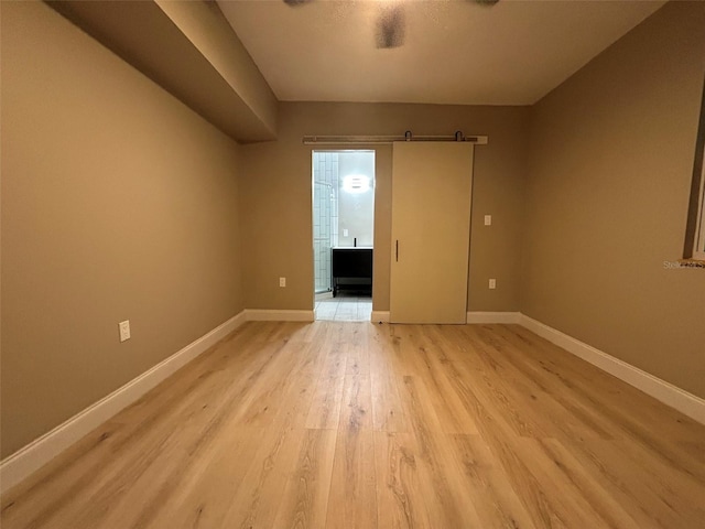 unfurnished room featuring light wood-type flooring, baseboards, and a barn door