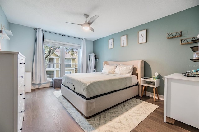 bedroom with ceiling fan, a textured ceiling, baseboards, and wood finished floors