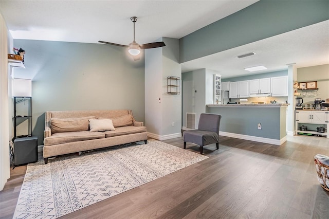 living area with ceiling fan, wood finished floors, visible vents, and baseboards