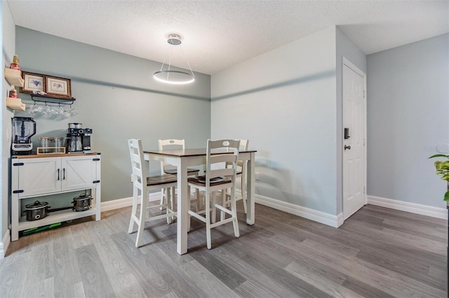 dining room featuring light wood-style flooring, baseboards, and a textured ceiling