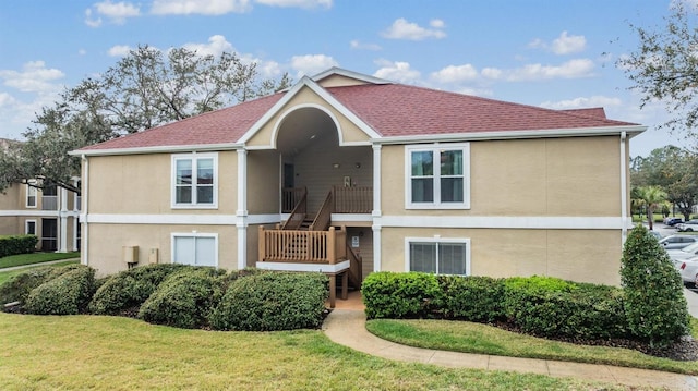 view of front of house featuring a shingled roof, stairs, a front lawn, and stucco siding