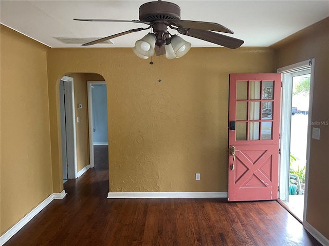 spare room featuring dark wood-style floors, baseboards, arched walkways, and a textured wall