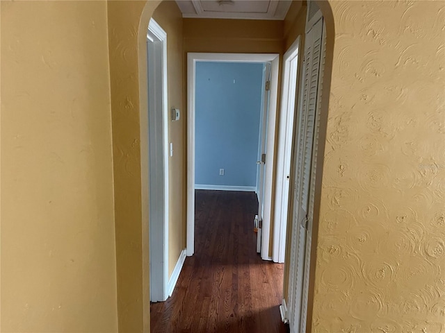 corridor featuring arched walkways, a textured wall, wood finished floors, and baseboards