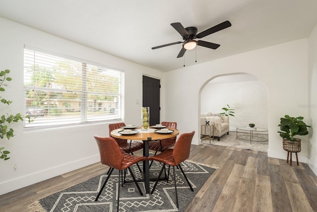 dining space with a ceiling fan, arched walkways, baseboards, and wood finished floors