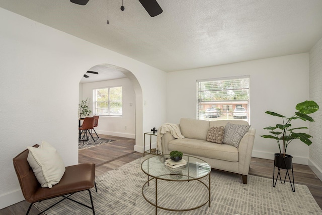 living room with arched walkways, ceiling fan, a textured ceiling, wood finished floors, and baseboards