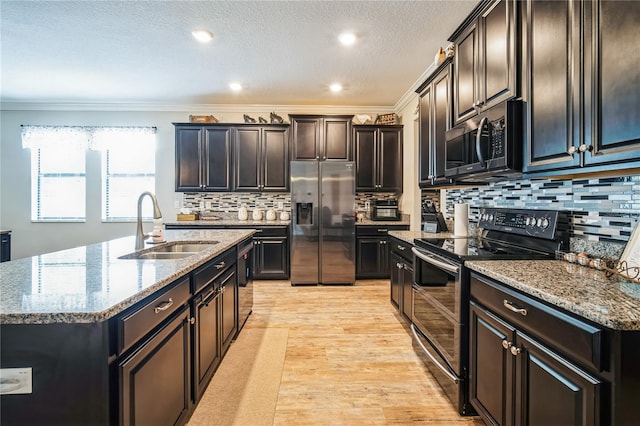 kitchen with a kitchen island with sink, stainless steel appliances, a sink, light wood-type flooring, and light stone countertops