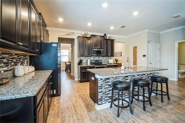 kitchen featuring stainless steel appliances, an island with sink, a sink, and light stone countertops