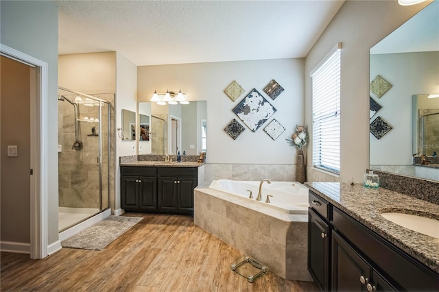 full bath with wood finished floors, two vanities, a sink, a bath, and a stall shower