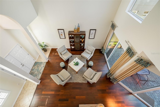 living area with arched walkways, wood finished floors, a towering ceiling, and baseboards