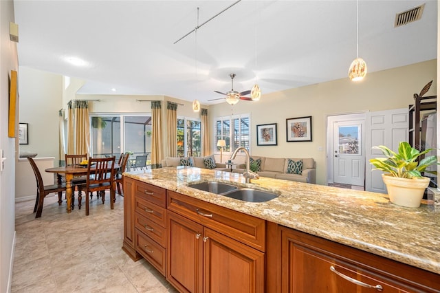 kitchen with a sink, visible vents, open floor plan, brown cabinets, and light stone countertops