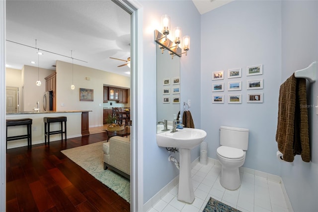 bathroom with ceiling fan with notable chandelier, wood finished floors, toilet, and baseboards