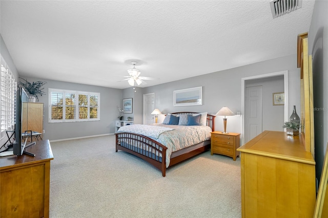 bedroom with ceiling fan, a textured ceiling, light carpet, visible vents, and baseboards