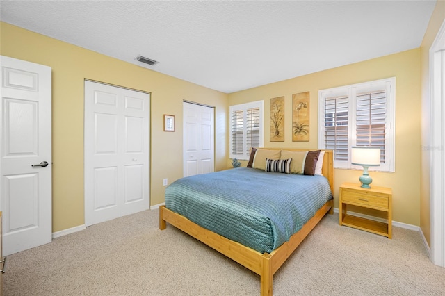 bedroom featuring a textured ceiling, light colored carpet, visible vents, baseboards, and a closet