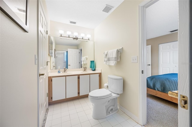 ensuite bathroom featuring toilet, double vanity, visible vents, and a textured ceiling