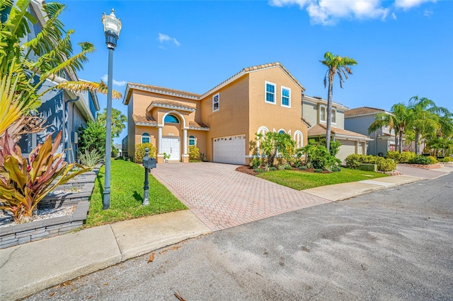 mediterranean / spanish house featuring a garage, a tiled roof, decorative driveway, stucco siding, and a front lawn