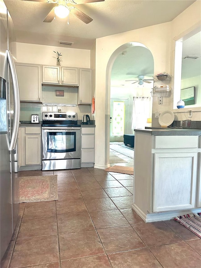 kitchen with arched walkways, stainless steel appliances, tasteful backsplash, and dark countertops