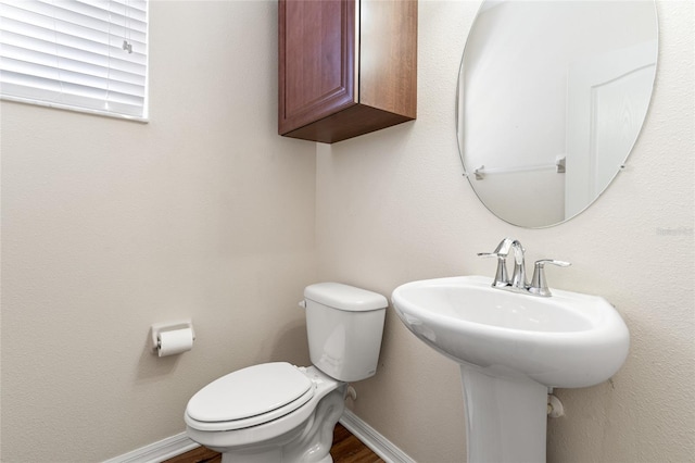 half bathroom featuring wood finished floors, toilet, and baseboards