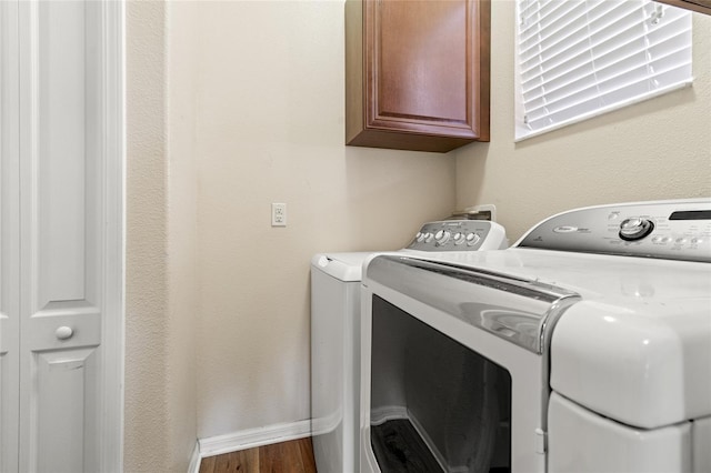 washroom featuring washing machine and dryer, cabinet space, baseboards, and wood finished floors