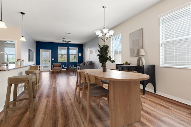 dining space featuring ceiling fan with notable chandelier, wood finished floors, visible vents, and baseboards