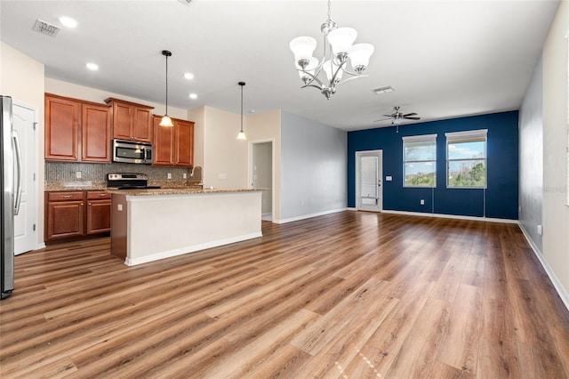 kitchen with an island with sink, appliances with stainless steel finishes, brown cabinets, open floor plan, and pendant lighting