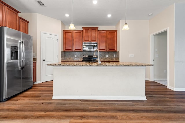 kitchen featuring stainless steel appliances, pendant lighting, visible vents, and a center island with sink