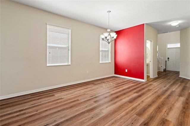 spare room featuring baseboards, wood finished floors, and a notable chandelier