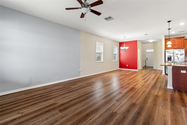 unfurnished living room with dark wood-style floors, ceiling fan with notable chandelier, visible vents, and baseboards