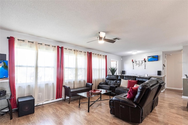 living room with a ceiling fan, a textured ceiling, visible vents, and wood finished floors