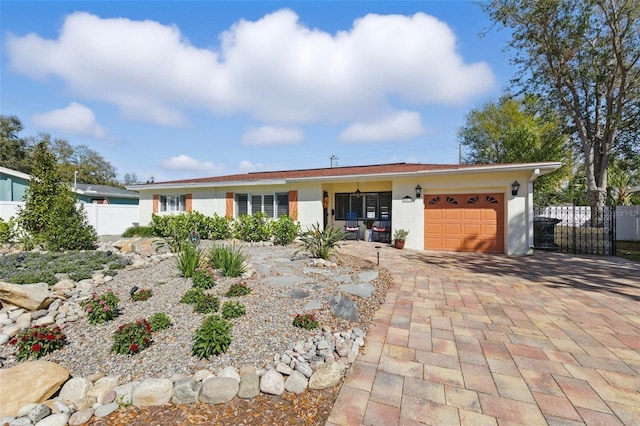 ranch-style house featuring a garage, decorative driveway, fence, and stucco siding