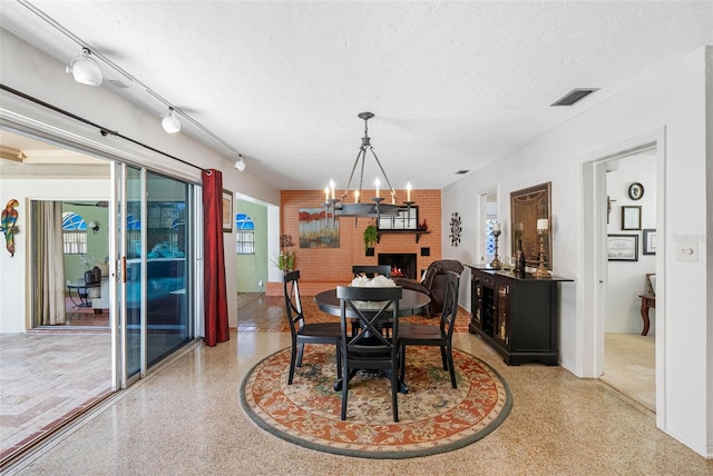 dining area with visible vents, a textured ceiling, speckled floor, a fireplace, and a notable chandelier