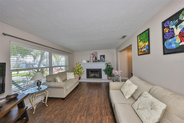 living area with dark wood-style floors, visible vents, a fireplace with raised hearth, and a textured ceiling