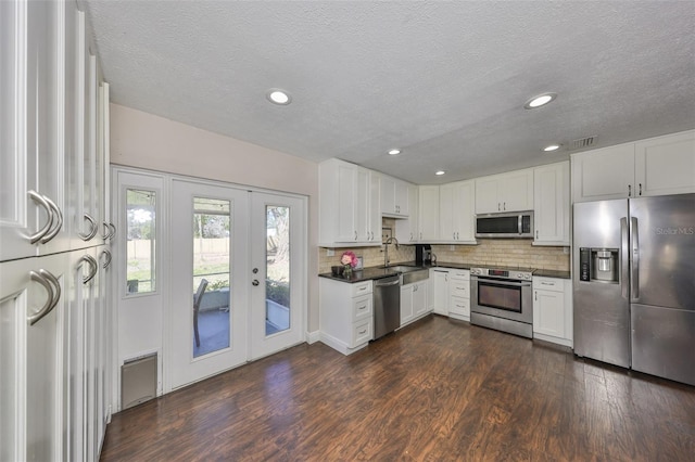 kitchen featuring stainless steel appliances, white cabinetry, backsplash, dark countertops, and dark wood finished floors