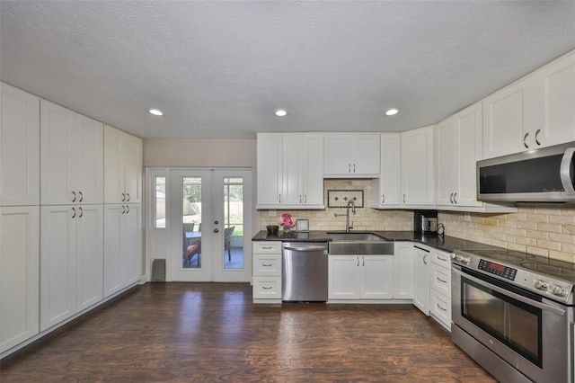 kitchen with tasteful backsplash, white cabinets, appliances with stainless steel finishes, dark wood-style flooring, and a sink