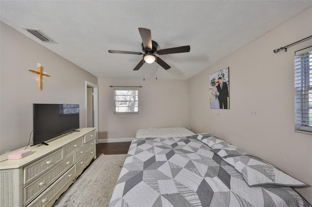 bedroom with dark wood-style floors, visible vents, a ceiling fan, a textured ceiling, and baseboards