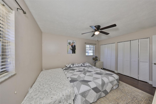 bedroom with a textured ceiling, a ceiling fan, dark wood finished floors, and multiple closets