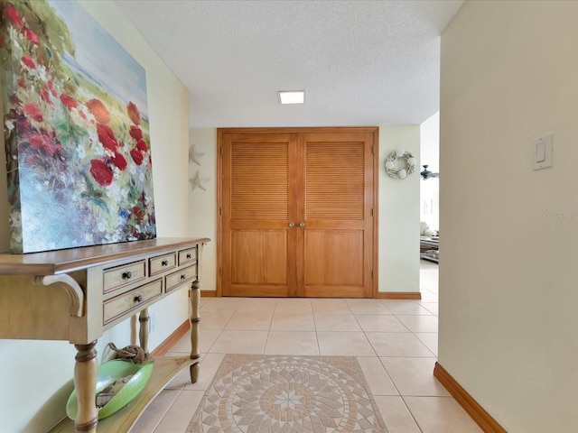 foyer entrance with a textured ceiling, light tile patterned flooring, and baseboards