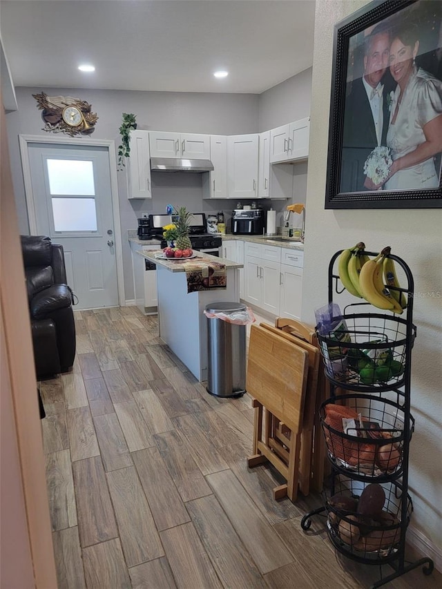 kitchen featuring white cabinets, light wood-style flooring, a kitchen island, under cabinet range hood, and a sink