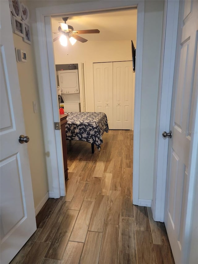 bedroom with ceiling fan, dark wood-style flooring, baseboards, multiple closets, and stacked washer and clothes dryer