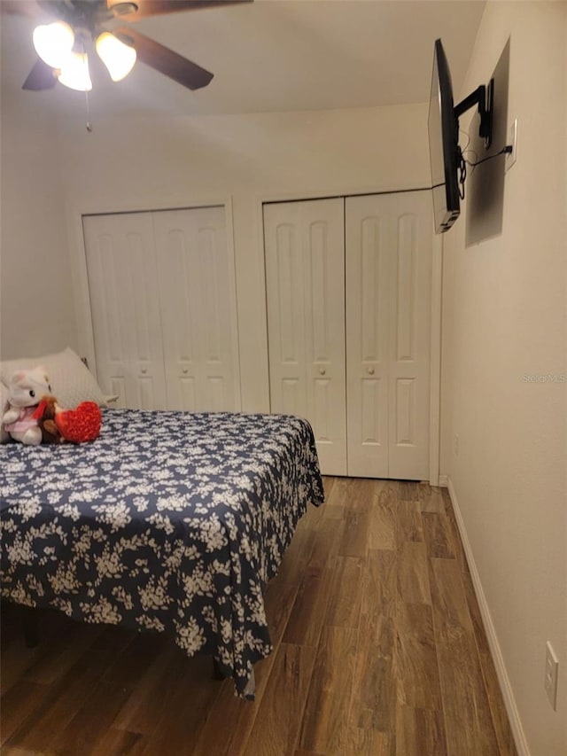 bedroom with baseboards, ceiling fan, wood finished floors, and multiple closets