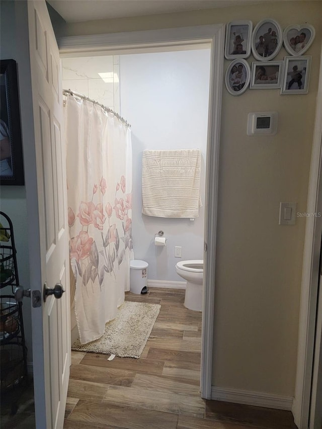 full bathroom featuring a shower with curtain, wood finished floors, toilet, and baseboards