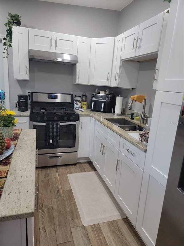 kitchen with light wood finished floors, gas stove, white cabinets, and under cabinet range hood