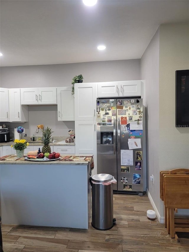 kitchen featuring stainless steel fridge, baseboards, wood finished floors, white cabinetry, and a sink