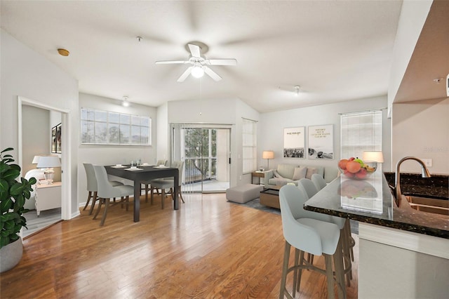 interior space with dark stone counters, light wood-style flooring, vaulted ceiling, a kitchen bar, and a sink