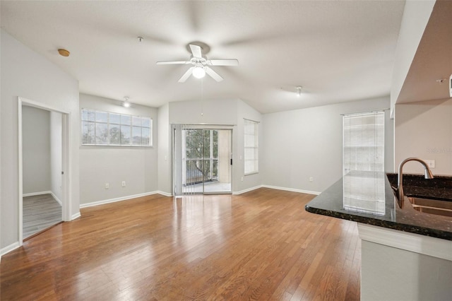 unfurnished living room with ceiling fan, lofted ceiling, a sink, baseboards, and light wood-style floors