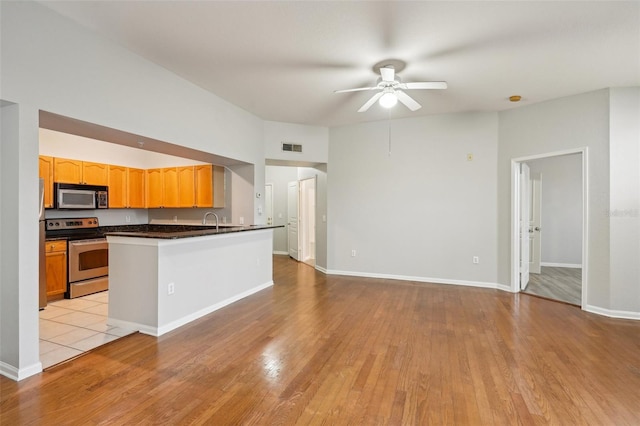 kitchen with light wood finished floors, dark countertops, visible vents, appliances with stainless steel finishes, and ceiling fan