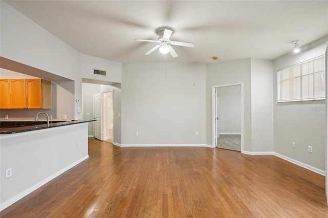 unfurnished living room with baseboards, wood finished floors, visible vents, and a ceiling fan