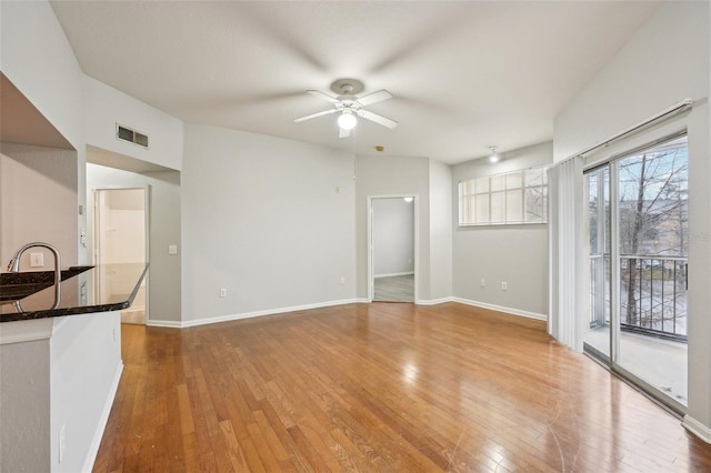 unfurnished living room featuring hardwood / wood-style floors, a ceiling fan, visible vents, and baseboards