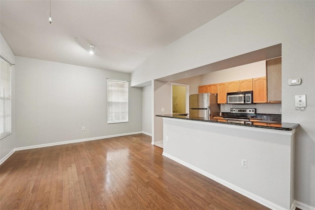 kitchen featuring vaulted ceiling, appliances with stainless steel finishes, dark countertops, and wood finished floors